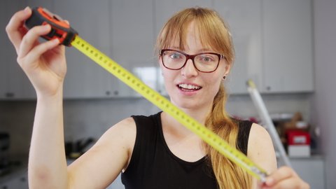 Blonde girl with glasses and provocative look expresses surprise closing a measuring yellow tape, implies something else