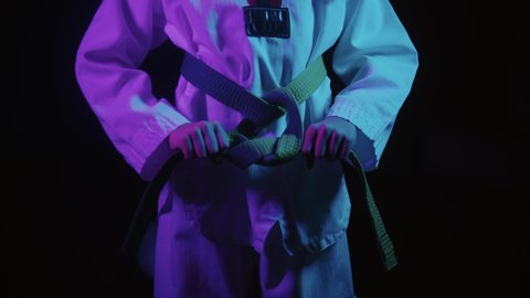 A little boy doing taekwondo in neon lighting - tying up his green belt and waving his hand