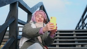 Blogger woman in warm clothes records selfie video by her phone. Traveling blogger talks to the camera, 4k 60p