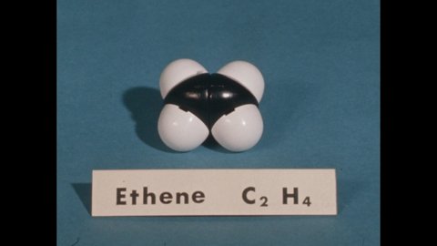 1960s: A cloudy gas in a distilling flask with a pipette on the side and a liquid above. End of the pipette is lit with a match and a flame appears. Slate. Model of a ethene molecule.