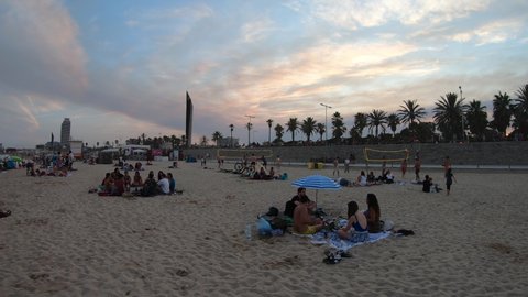 BARCELONA, SPAIN  JULY 2021: Sunset view of Playa de Bogatell, famous beach of Barcelona, Spain. Spanish people swimming, tourists relaxing and playing beach volley on summer vacation at dusk