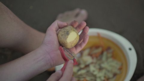 Man peels potatoes from the peel into a large bowl while sitting on the sand. Outdoor cooking