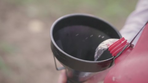 Man pours gasoline from a red canister through a funnel. Close-up