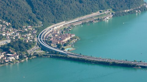 Timelapse, aerial view on cars and trains traffic in Swiss Alpine town near lake. Melide causeway, Bissone, Lake Lugano, Canton Ticino, Switzerland
