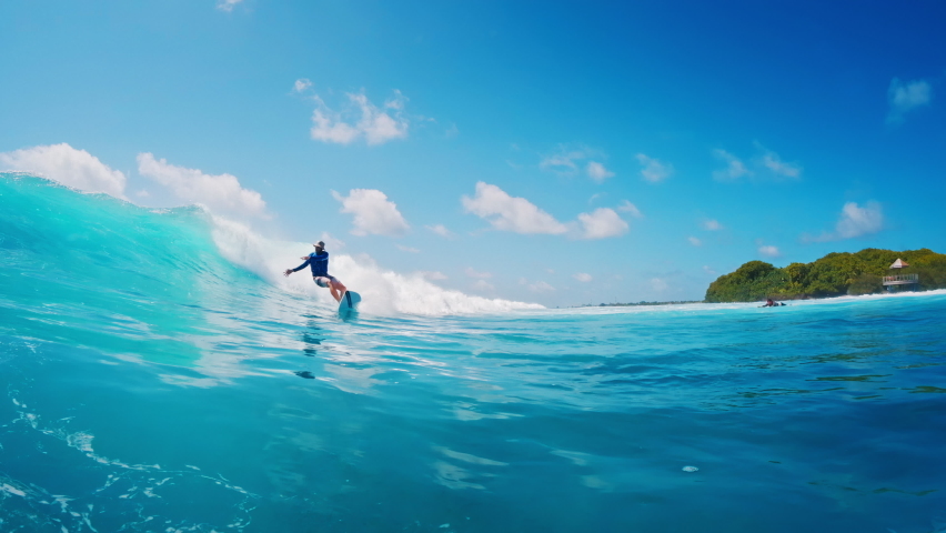 Pro surfer rides the wave. Man surfs the perfect blue wave during sunny day in Maldives
