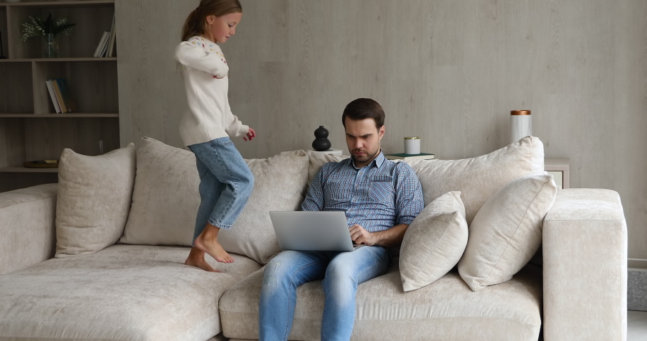 Serious dad work from home try to focus attention on pc screen read document online do business task while mischievous little girl jump on couch near. Small daughter behave bad disrupt job of father Royalty-Free Stock Footage #1083529942