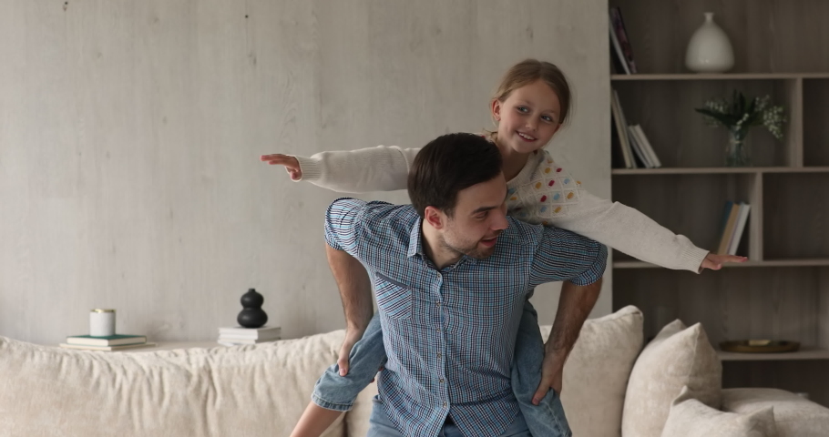 Caring single father giving ride on his back to joyful small girl daughter acting horse riding traveler at living room. Grownup elder brother piggybacking little sister child playing cute funny game Royalty-Free Stock Footage #1083529948