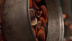 Vertical format video. Cooking traditional drink from red wine and citrus for Christmas. Hands cut grapefruit and put red citrus slices into old cauldron of mulled wine. Holiday gluhwein preparation