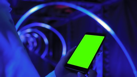 Green screen, template, chroma key, immersive, technology concept. Woman hands holding smartphone device with green display at interactive exhibition or museum with blue illumination - close up