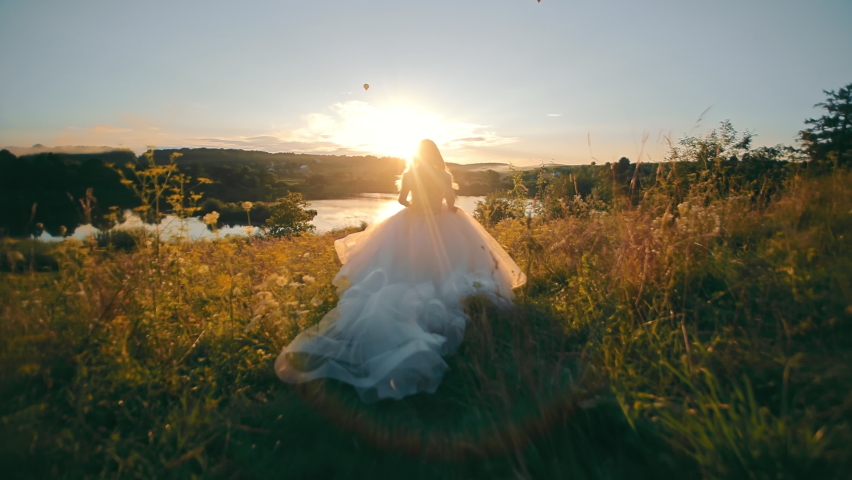 Pretty bride running to the lake on a background of sunset. Moranrange sunset and rays on the backlight. young woman in long chiffon dress