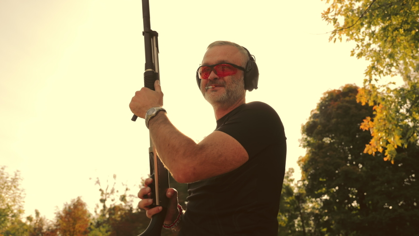 A male shooter holds a shotgun in his hands and reloads it. Silhouette of a hunter illuminated by sunlight. Man with a cigarette in his mouth.