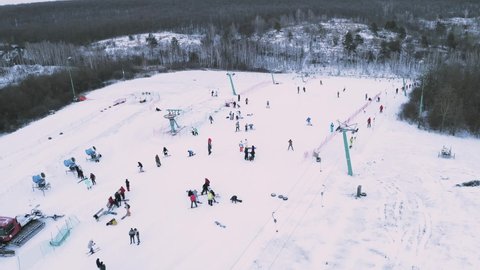 Skiers and snowboarders skiing on snow slopes with ski lift. Drone flying over snowy Slope with Skiers and Snowboarders at Ski Resort on a frosty winter day: drone view.