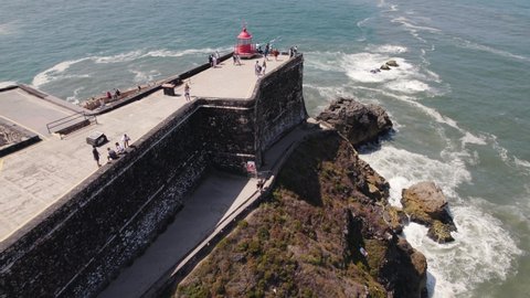 Tourists at Nazare red lighthouse at Saint Michael the Archangel fort in Portugal. Aerial circling view