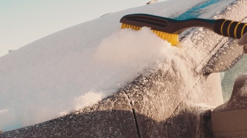 A close-up of a thick layer of snow on the windshield of a car is brushed off with a brush. Before driving to work in the Nordic countries, the machine must be free of snow and ice.