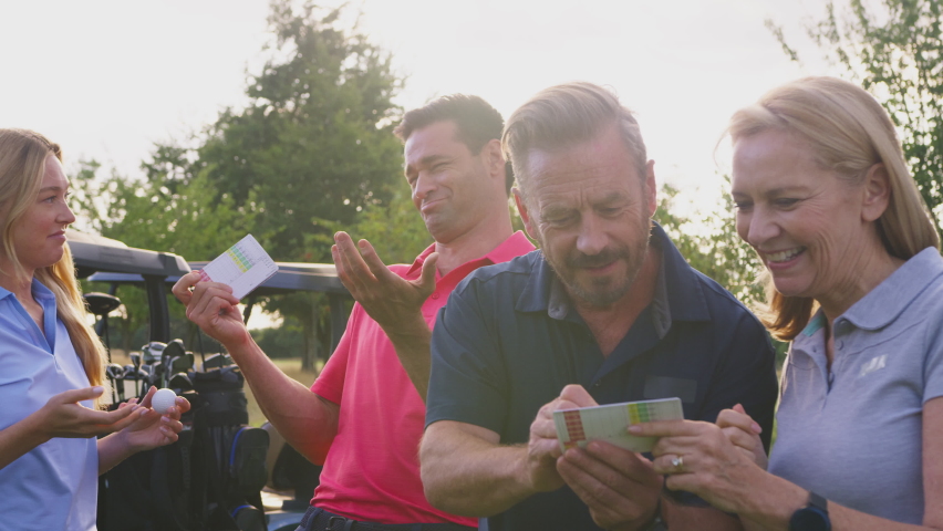 Mature and mid adult couples standing by golf buggy checking score cards together -= shot in slow motion