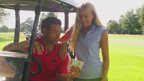Couple playing round of golf with man sitting in buggy checking score card being joined by woman putting club into bag - shot in slow motion