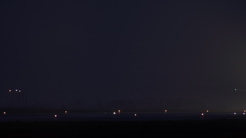 Slow video as a passenger plane takes off from the airport runway at night. Airplane headlight in foggy weather and wheels that come off the ground. Royalty-Free Stock Footage #1083556687