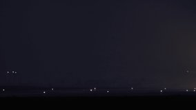 Slow video as a passenger plane takes off from the airport runway at night. Airplane headlight in foggy weather and wheels that come off the ground.