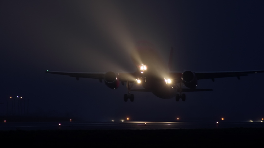 Slow video as a passenger plane takes off from the airport runway at night. Airplane headlight in foggy weather and wheels that come off the ground. | Shutterstock HD Video #1083556687