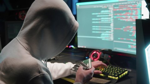 A masked hacker breaks into a database on a computer, hacking in a dark room