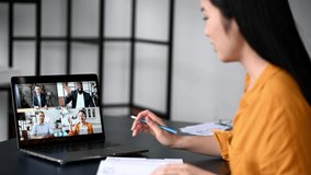 Video call, online conference using app and laptop. Satisfied asian female student or freelancer, studies or works remotely, watches an online lecture, takes notes, multiracial people on laptop screen