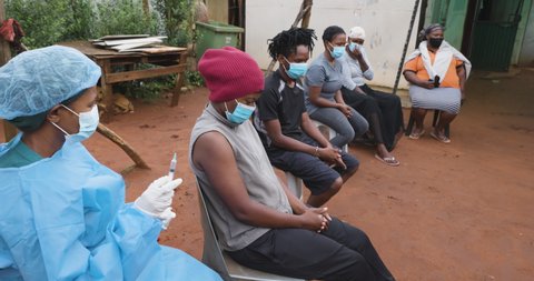 Black African people line up for Covid-19 vaccine in a rural settlement. Black female nurse administers vaccine.