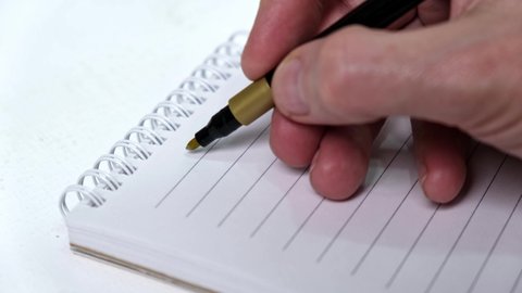 4K A close-up of a man's hand writes the numbers 2022 with a gold felt-tip pen in a notebook. The concept of planning, motivation and setting goals for the coming year.