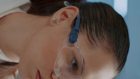 Vertical video: Scientific worker wearing safety goggles in laboratory, working on biochemistry development with research equipment. Portrait of woman biologist with glasses in science lab. Close up