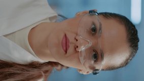 Vertical video: Portrait of woman scientist with goggles smiling in laboratory, getting ready to work on science experiment and development. Microbiology researcher wearing safety glasses in lab