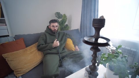 Rest and relaxation concept. Man smokes a hookah in room of home interior