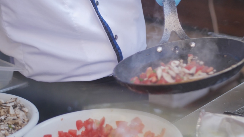 A close-up of a restaurant chef cooking on fire in an outdoor kitchen, he mixes vegetables in a frying pan and they burn. All-inclusive meals at the hotel. Royalty-Free Stock Footage #1083568600