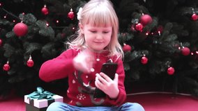 Smiling blond girl using smart phone talking to family congratulates Merry Christmas by video call.
