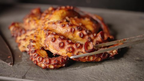Golden brown crispy perfectly sealed octopus, chef transferring cut tentacle to the side before plating.