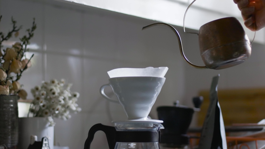 Copper kettle pours water through V60 coffee filter into glass server (carafe).
