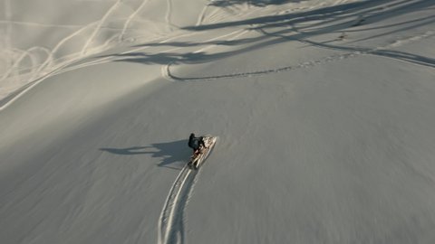 Aerial view man slowly downhill riding on snowmobile surrounded by snowy slope Mamdziskha mountain sport FPV drone. Enjoying speed driving at wilderness nature landscape Black Sea Abkhazia sunny day