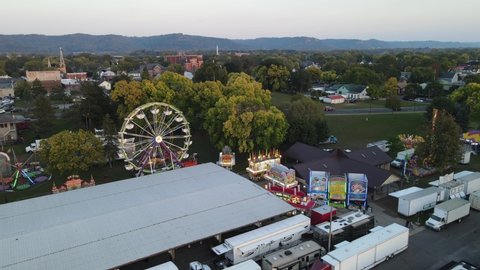 Sunset view of festival grounds with carnival rides and games in La Crosse, Wisconsin. Park shelter housing some games. Multiple trucks and campers parked on road. 