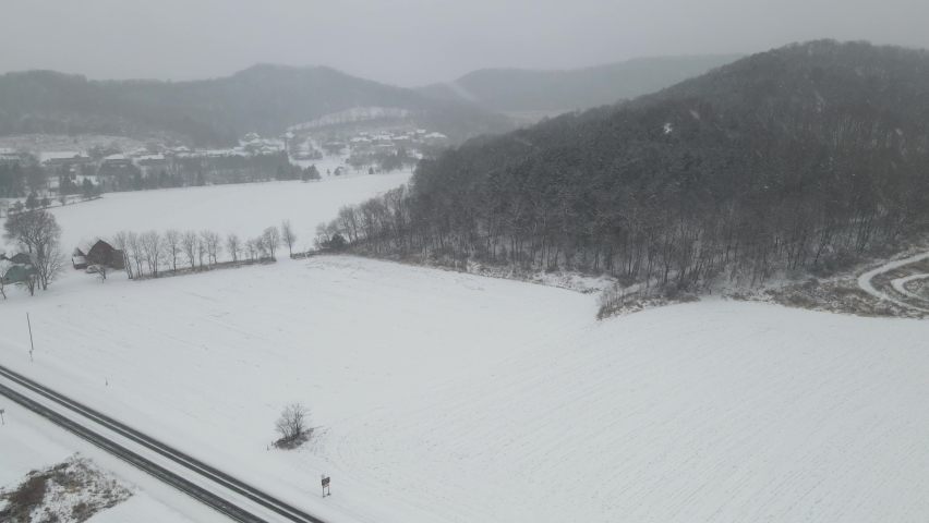 Western Wisconsin snowfall in the valley. Mountains with forest and trails. Highway running through farmland. Single directional sign. 