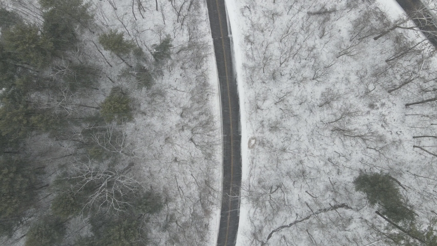 Top down view of road going through forest in Wisconsin. Snowy forest on mountainside. Leafless trees and pine trees present. 