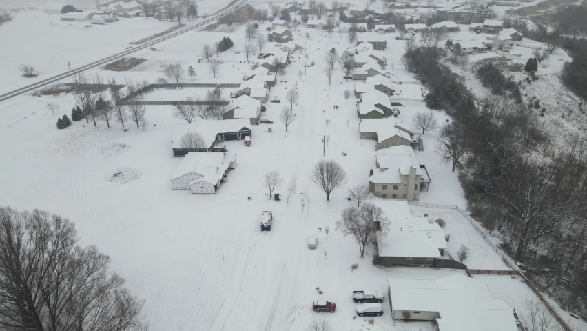 Snow falling over rural neighborhood in valley in Wisconsin. Single family homes on each side of snow covered street. Highway separating farm from houses. New construction of homes. 