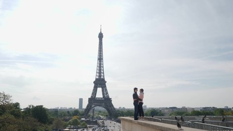 Lovely newlywed couple kisses hugging standing on parapet against Eiffel Tower at wedding journey on old Paris street in spring