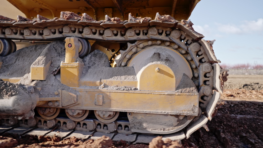 Tracking shot of crawler bulldozer working on construction site or quarry. Mining machinery moving clay, smoothing gravel surface for new road. Earthmoving, excavations, digging on soils.