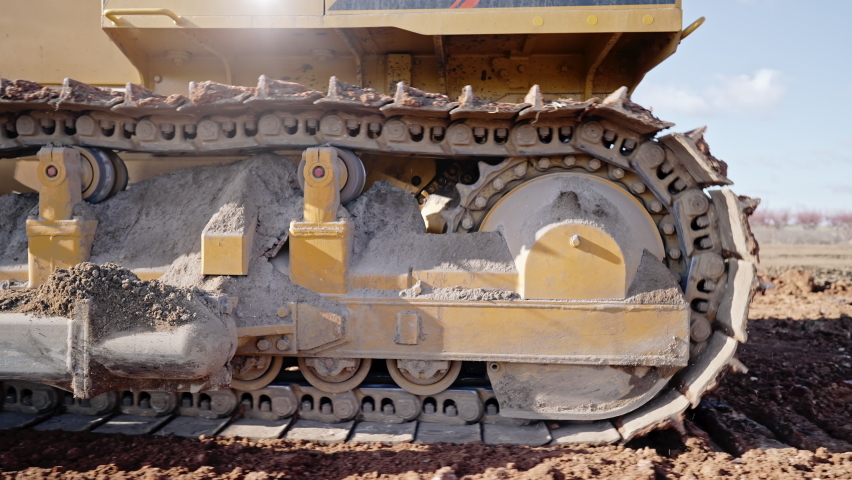 Tracking shot of crawler bulldozer working on construction site or quarry. Mining machinery moving clay, smoothing gravel surface for new road. Earthmoving, excavations, digging on soils.