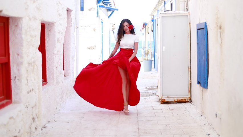 Happy woman in red long skirt and with a red flower in her hair. Young woman is wearing red dress enjoying her Europe vacation