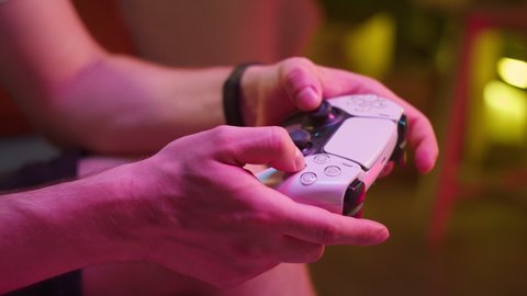 Man gamer hands holding modern console for play station close-up, guy playing video games. Neon light in gaming club. Shooting of male arms with remote controller. Professional cybersport. 