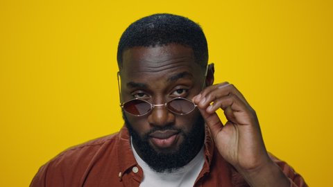 Portrait handsome man sending air kiss on yellow background. Closeup african american man blowing air kiss from hand to camera. Smiling model in sunglasses flirting camera in studio. Playful person