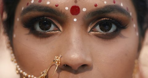 Close up of Expressive big Brown Indian Woman's eyes with Traditional Bindi. Attractive Hindu Appearance of young Girl with golden Kundan jewelry looking into camera. Ethnic Female. Pandemic India.