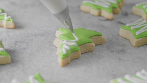 Christmas sugar cookies in tree and star shape being decorated with royal icing in kitchen in slow motion. 