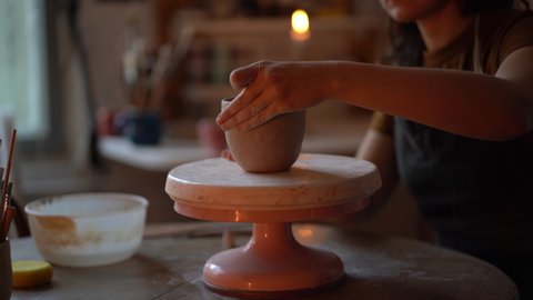 Handmade ceramics creation. Process of shaping and moulding pottery vase in studio with concentrated young female artist busy at work. Woman ceramist sculpturing clay jug on wheel in workshop space
