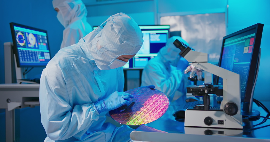 Asian male technician in clean room suit holds wafer that reflects many different colors with gloves and check it at semiconductor manufacturing plant | Shutterstock HD Video #1083600502