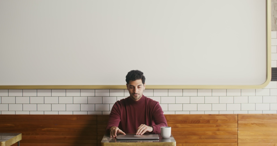 Young handsome black haired man, with easy unshaven opening the laptop lid getting ready to start work while drinking coffee at a small table in a cozy coffee shop | Shutterstock HD Video #1083604912